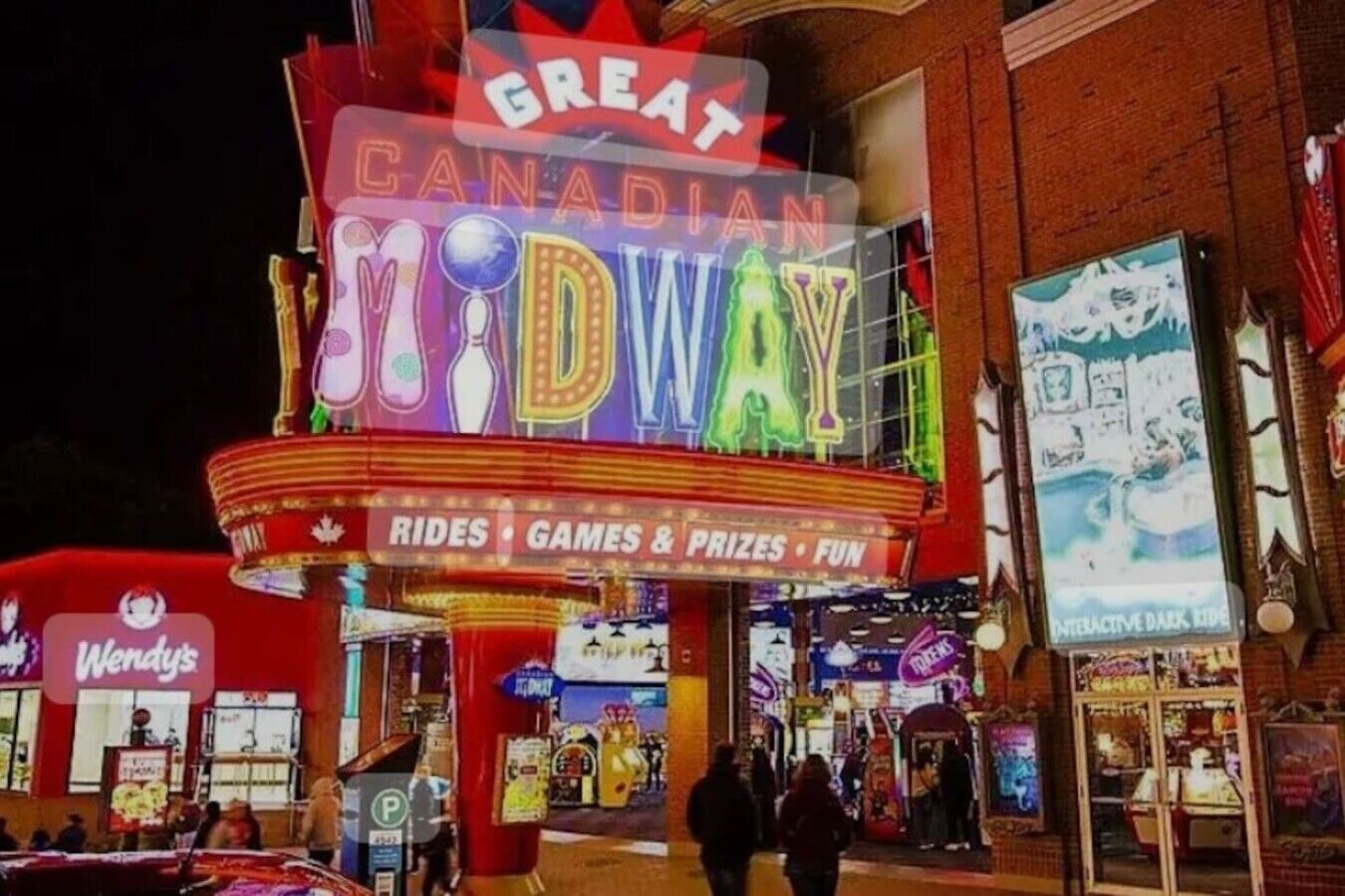 A brightly lit outdoor theater with neon signage for 'Great Canadian Midway' and a Wendy's fast-food restaurant adjacent to it.