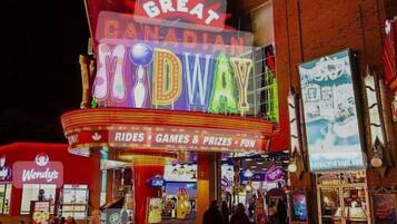 A brightly lit outdoor theater with neon signage for 'Great Canadian Midway' and a Wendy's fast-food restaurant adjacent to it.