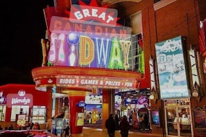 A brightly lit outdoor theater with neon signage for 'Great Canadian Midway' and a Wendy's fast-food restaurant adjacent to it.