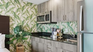 Een kleine keuken met houten kastjes, een roestvrijstalen koelkast, een magnetron en een gootsteen.