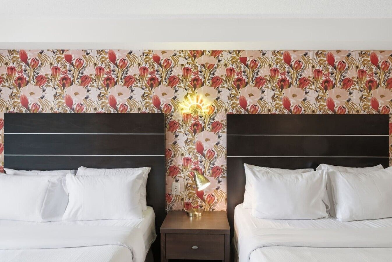 Une chambre d’hôtel avec deux lits, une table de chevet avec une lampe et un papier peint à motifs floraux.
