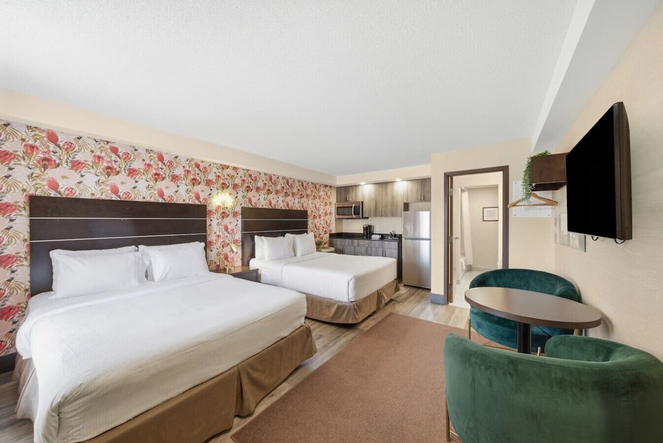 Une chambre d’hôtel avec deux lits, une kitchenette, un coin repas avec une table et des chaises, et un téléviseur fixé au mur.