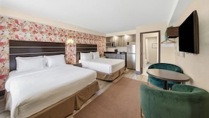 Een hotelkamer met twee bedden, een kitchenette, een eethoek met een tafel en stoelen, en een aan de muur bevestigde televisie.