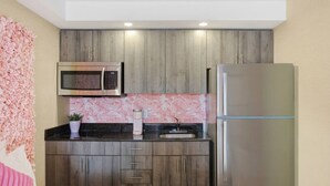 Een kleine keuken met een magnetron, koelkast en een wanddecoratie met roze bloemen.