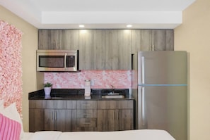 Una cocina compacta con microondas, refrigerador y un adorno floral rosa en la pared.