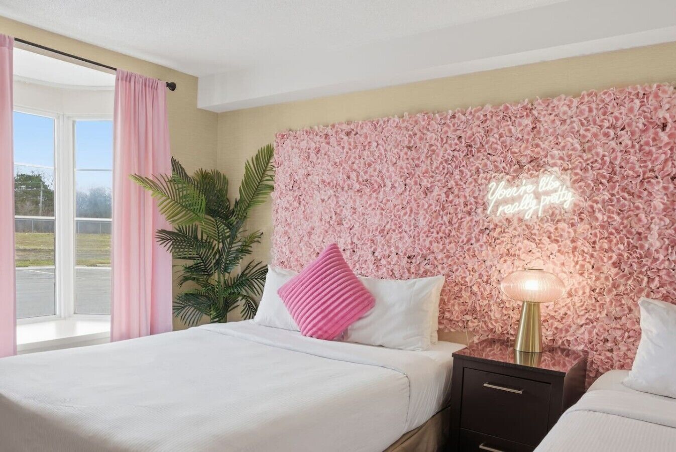 Une chambre d’hôtel avec un lit, une table de chevet, une lampe, une plante en pot et un mur orné d’un motif floral.