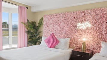 Une chambre d’hôtel avec un lit, une table de chevet, une lampe, une plante en pot et un mur orné d’un motif floral.