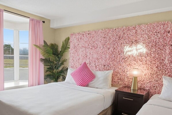 Una habitación de hotel con una cama, una mesita de noche, una lámpara, una planta en maceta y una pared con estampado floral.