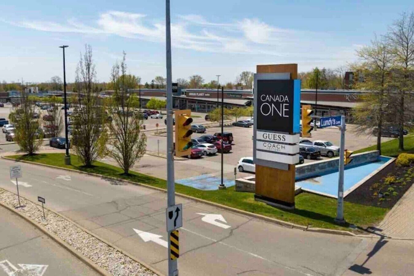 A parking lot with a sign for Canada One, Guess Coach, and a visible traffic light.