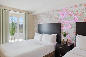 Ett hotellrum med en säng, sängbord, en neonreklamskylt formad som en flamingo och ett fönster med utsikt.