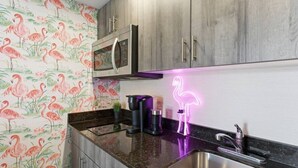 Een keuken met een roestvrijstalen spoelbak, een magnetron en een neon vlamingo bord.