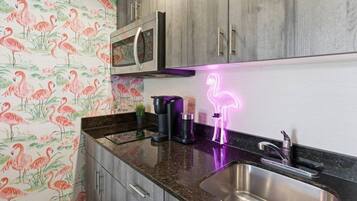 Een keuken met een roestvrijstalen spoelbak, een magnetron en een neon vlamingo bord.