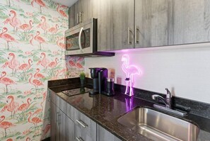 Una cocina con un lavamanos de acero inoxidable, un microondas y un letrero de neón con un flamenco.