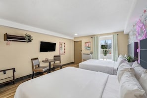 Habitación de hotel con dos camas, un televisor, un escritorio con sillas y un ventanal con cortinas.