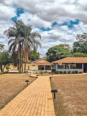 A paved pathway leading to a building with a tiled roof, surrounded by palm trees and greenery. - HOTEL FAZENDA SERTÃO VEREDA SETE LAGOAS  (Paraopeba)