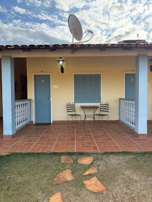 A building with a satellite dish, two doors, a table with chairs, and a small garden area. - HOTEL FAZENDA SERTÃO VEREDA SETE LAGOAS  (Paraopeba)