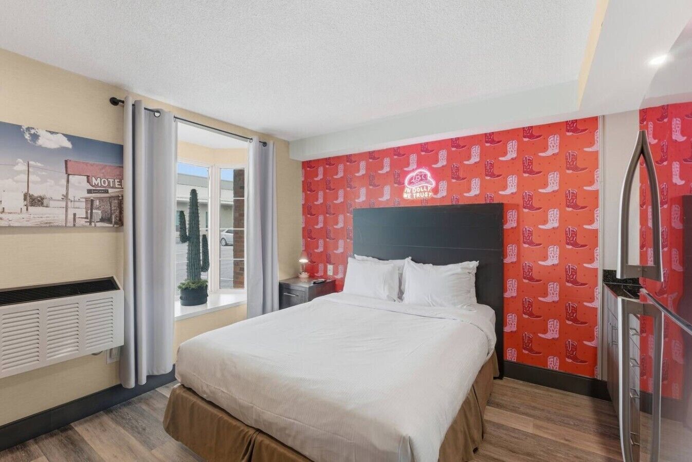 Une chambre d’hôtel avec un lit, une fenêtre donnant sur un immeuble, un mur orné d’un motif rouge et un plafond avec un luminaire.