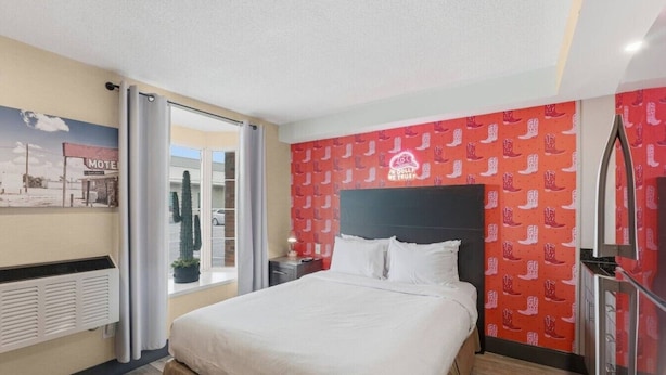 Een hotelkamer met een bed, een raam met uitzicht op een gebouw, een muur met een rood patroon, en een plafond met een lamp.
