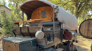 A vintage covered wagon with a wooden structure, a metal stove, and a storage box.