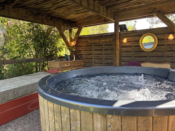 Un bain à remous avec un revêtement extérieur en bois, un banc en bois et un miroir fixé au mur.