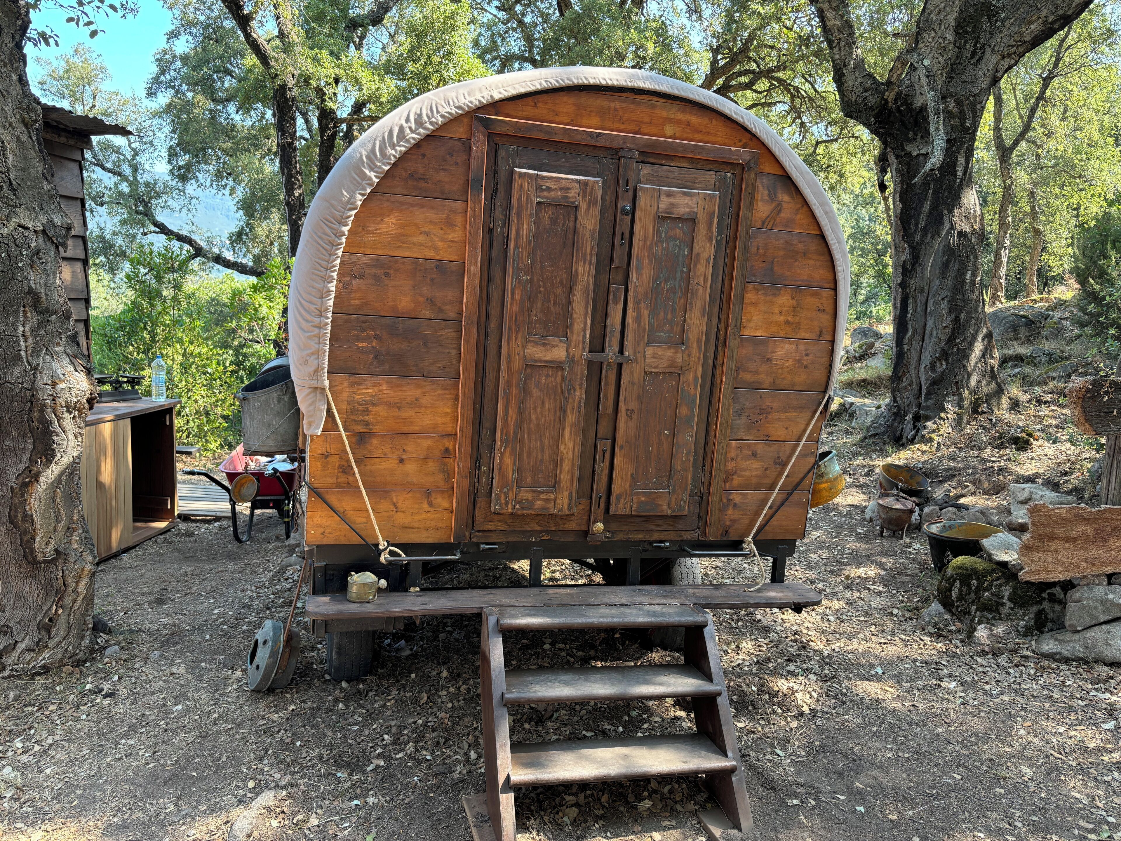 Une charrette en bois, avec une rampe menant à une porte, entourée d’arbres et bordée d’un chemin de gravier.