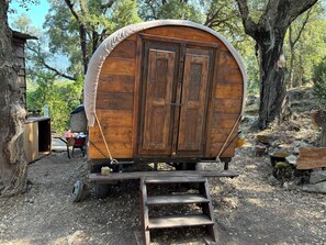 Une charrette en bois, avec une rampe menant à une porte, entourée d’arbres et bordée d’un chemin de gravier.