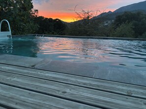 A swimming pool with a wooden deck in the foreground and a mountainous landscape in the background.