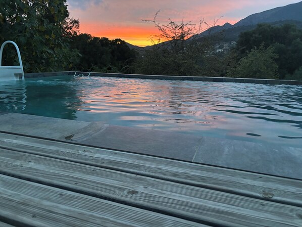 A swimming pool with a wooden deck in the foreground and a mountainous landscape in the background.