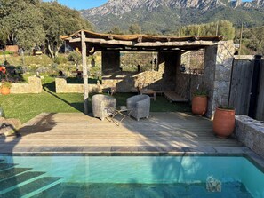 A wooden deck with outdoor furniture, a pergola, and a swimming pool.