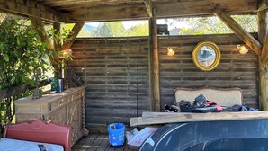 A covered outdoor area with a wooden ceiling, a wooden bench, a dresser, and a mirror on the wall.