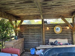 A covered outdoor area with a wooden ceiling, a wooden bench, a dresser, and a mirror on the wall.