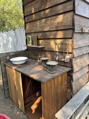 A rustic wooden outdoor kitchen with a sink, a stove, and various cooking utensils.