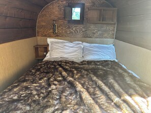 A bed with a patterned blanket, a wooden headboard, and a small window.