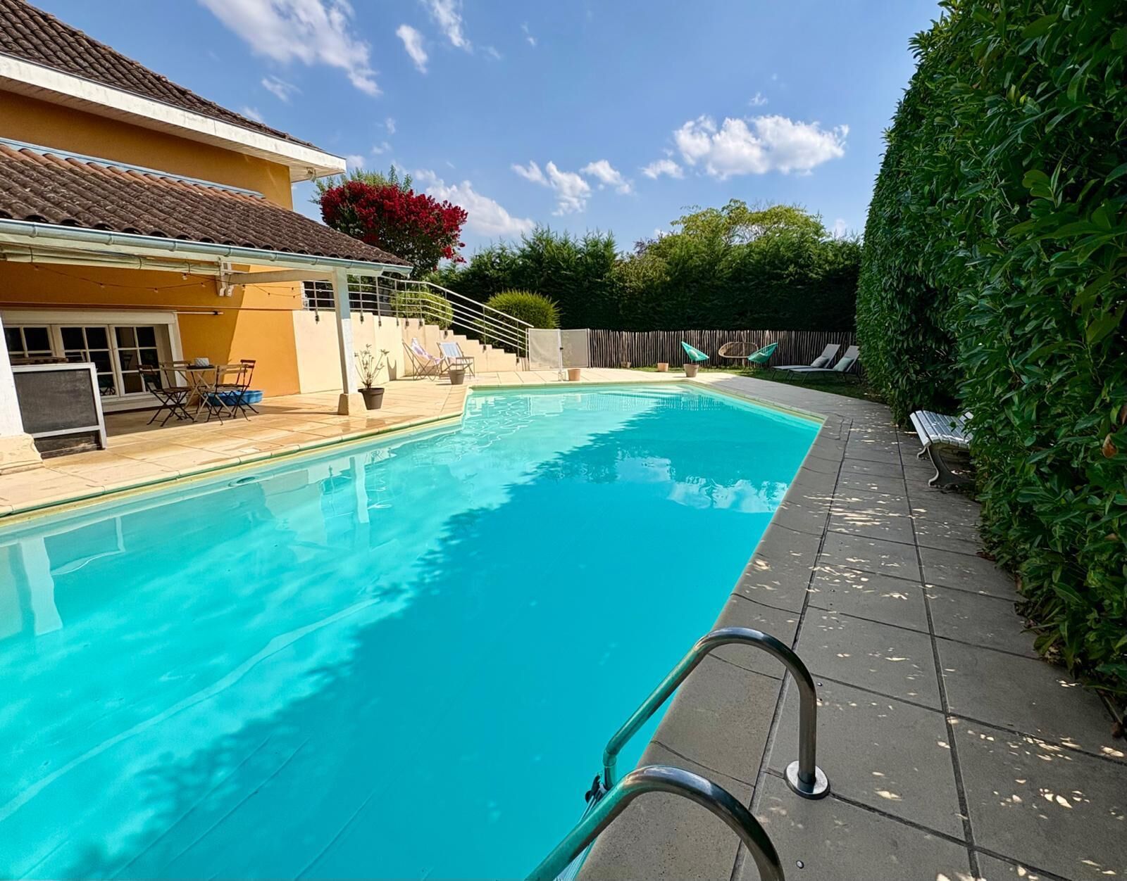 Une piscine avec une terrasse carrelée, un espace salon couvert et une clôture en bois.
