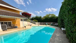 Una piscina con borde de baldosas, zona de estar cubierta y valla de madera.