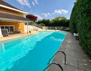 A swimming pool with a tiled deck, a covered seating area, and a wooden fence. - Vrbo Property (Parcieux)