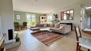 A spacious living room with a beige sofa, a coffee table, and a dining area with a wooden table and chairs.
