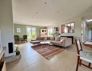 A spacious living room with a beige sofa, a coffee table, and a dining area with a wooden table and chairs.