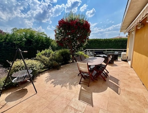 An outdoor patio with a table and chairs, surrounded by greenery and a hedge. - Vrbo Property (Parcieux)