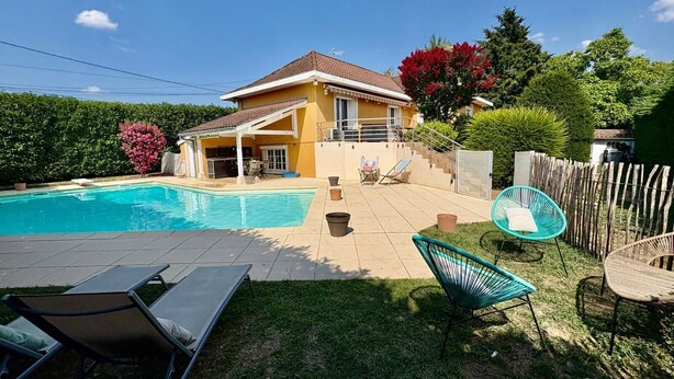 A residential property with a swimming pool, outdoor seating, and a covered patio area.