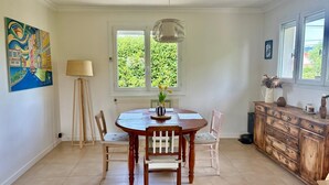 A dining area with a round table, chairs, a lamp, a radiator, and a window with a view of greenery.