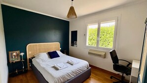 A bedroom with a bed, bedside tables, a chair, a window, and a wall-mounted heater.