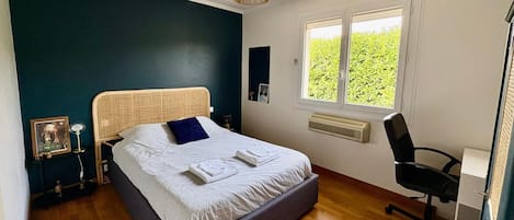 A bedroom with a bed, bedside tables, a chair, a window, and a wall-mounted heater.