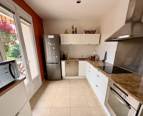A modern kitchen with a built-in oven, a stainless steel refrigerator, and a countertop with a sink. - Vrbo Property (Parcieux)