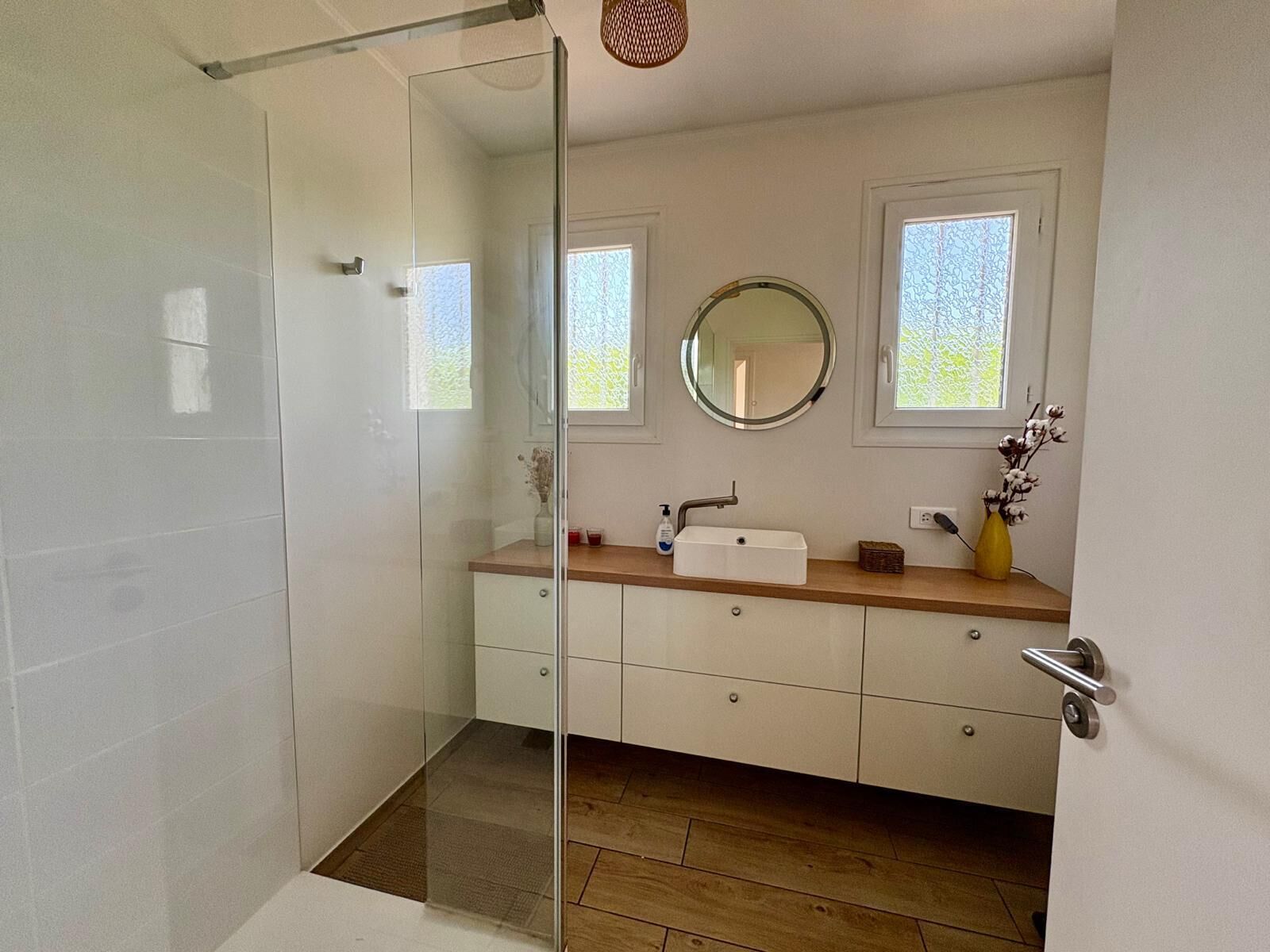 A modern bathroom with a glass shower enclosure, a white sink with a mirror above it, and wooden cabinets.