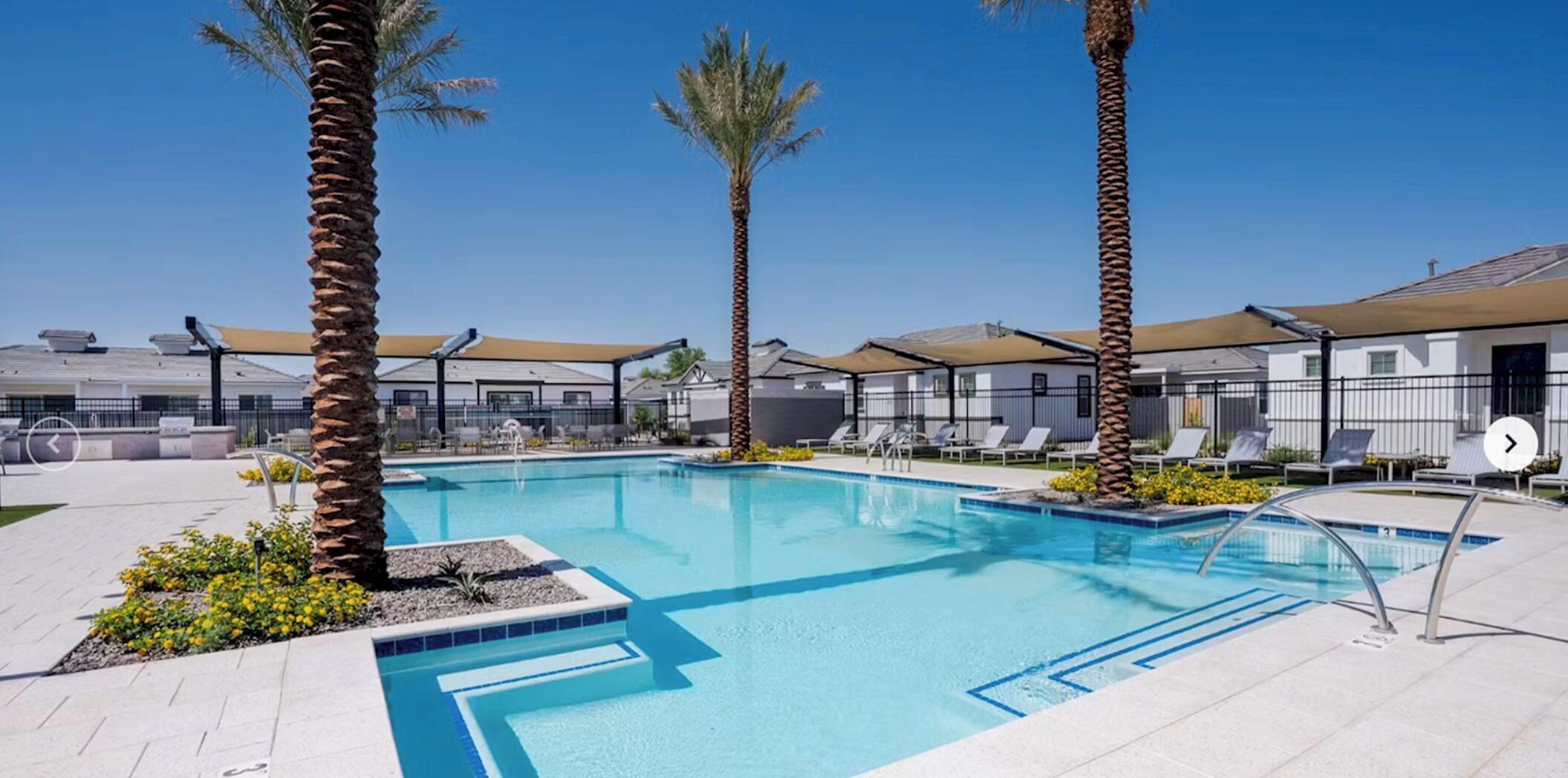 A swimming pool with lounge chairs and palm trees, surrounded by buildings with a modern design.