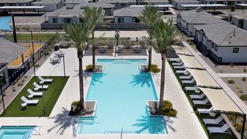 Zona residencial con piscina rodeada de sillones de descanso y palmeras.