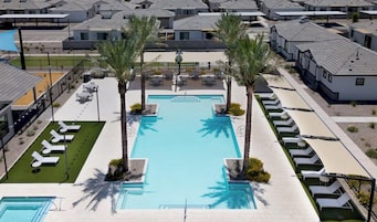 Área residencial com piscina, cadeiras de descanso e palmeiras.