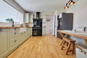 A kitchen with wooden flooring, white cabinets, a black oven, and a stainless steel refrigerator. - Gralyn Place (Winchelsea)
