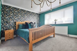 A bedroom with a wooden bed, a nightstand, a radiator, and a window with blinds. - Gralyn Place (Winchelsea)